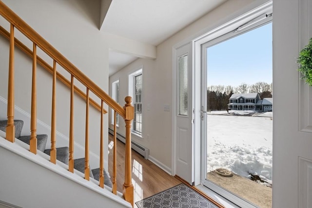 entrance foyer featuring stairs, a baseboard heating unit, a wealth of natural light, and wood finished floors