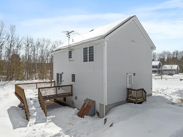 snow covered rear of property with a garage and a deck