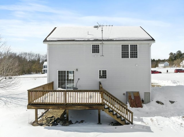 snow covered house with stairway and a wooden deck