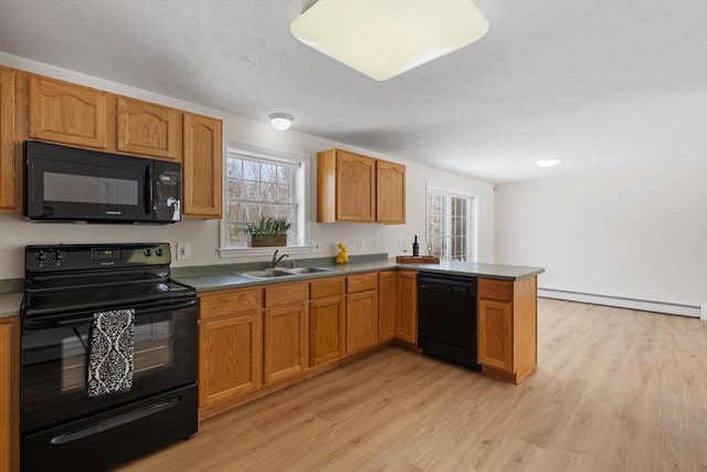 kitchen featuring a baseboard heating unit, a peninsula, a sink, black appliances, and light wood finished floors