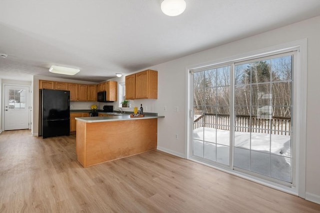 kitchen featuring black appliances, brown cabinetry, a peninsula, and light wood-style flooring