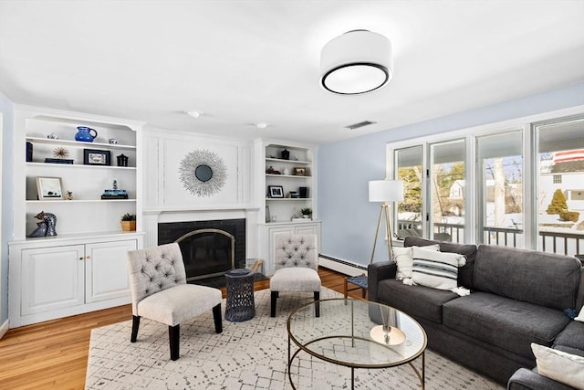 living area featuring visible vents, built in features, baseboard heating, light wood-type flooring, and a brick fireplace