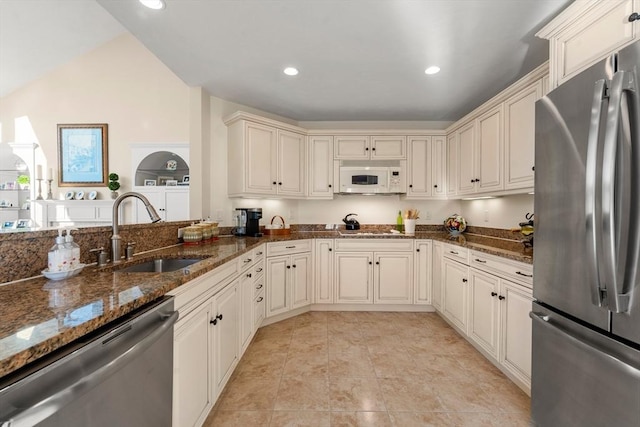 kitchen featuring lofted ceiling, sink, appliances with stainless steel finishes, and dark stone counters