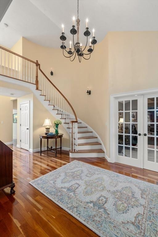 stairway featuring hardwood / wood-style floors, a notable chandelier, a high ceiling, and french doors