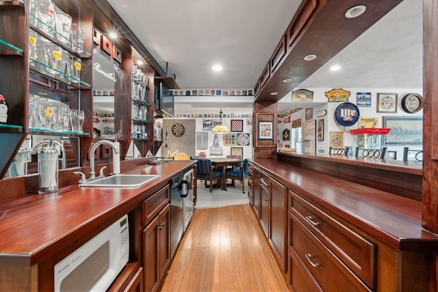 bar featuring dishwashing machine, sink, and light wood-type flooring