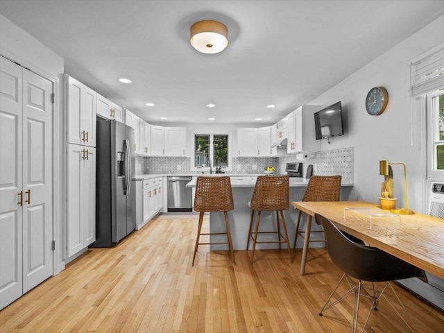 168 Maple St, Boston, MA 02132 - kitchen with appliances with stainless steel finishes, light wood-type flooring, a peninsula, white cabinets, and backsplash