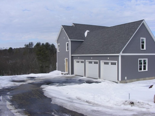 snow covered property with roof with shingles and an attached garage