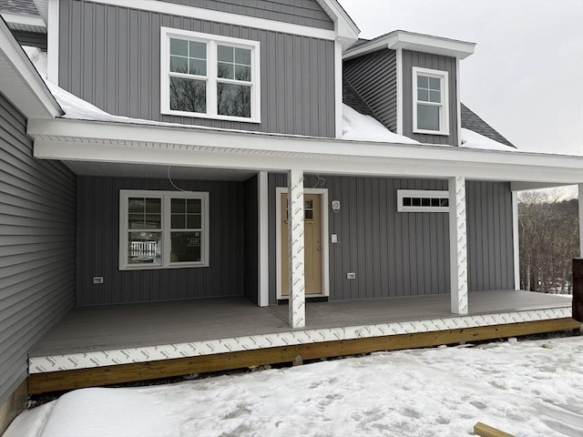 snow covered property entrance featuring a porch and board and batten siding