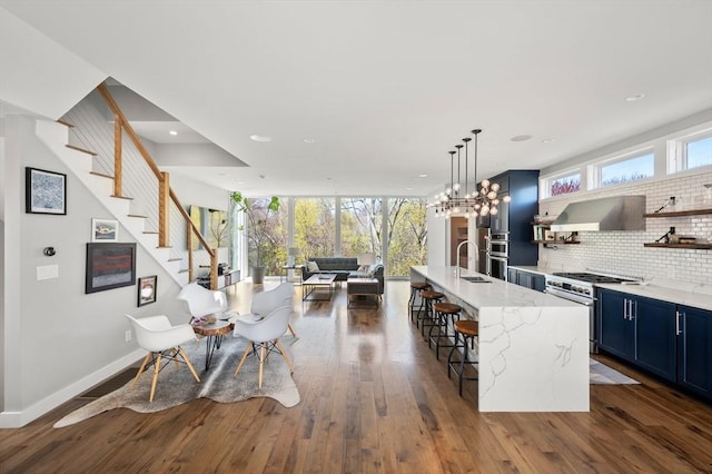 kitchen featuring decorative backsplash, open floor plan, wall chimney range hood, high end stove, and blue cabinets