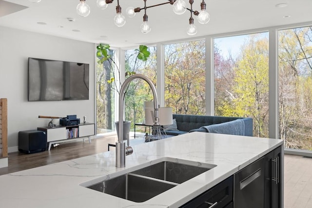 kitchen featuring light stone countertops, open floor plan, dark cabinetry, expansive windows, and a sink