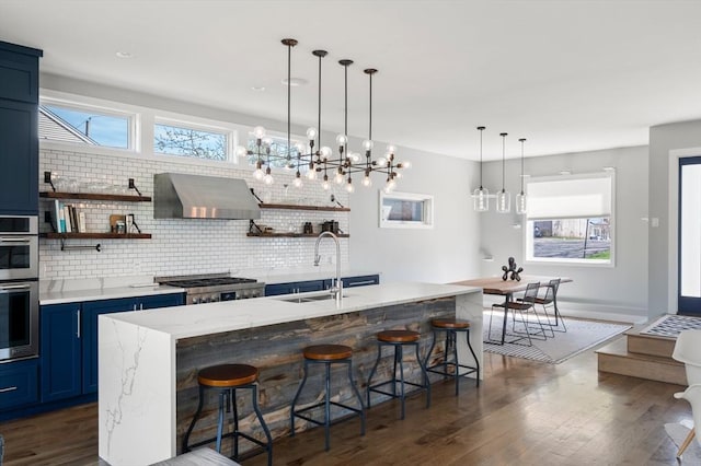 kitchen featuring a kitchen breakfast bar, blue cabinetry, dark wood finished floors, a sink, and wall chimney exhaust hood