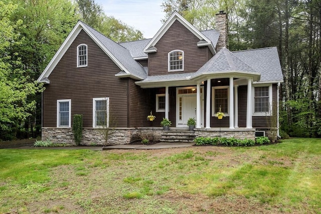 view of front facade featuring covered porch, roof with shingles, a chimney, and a front yard