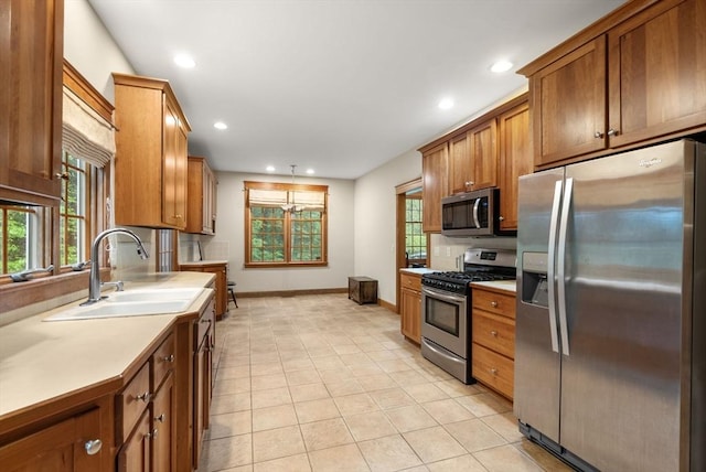 kitchen featuring appliances with stainless steel finishes, a sink, baseboards, brown cabinets, and light countertops