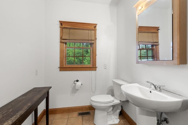 half bath featuring toilet, baseboards, tile patterned floors, and a sink