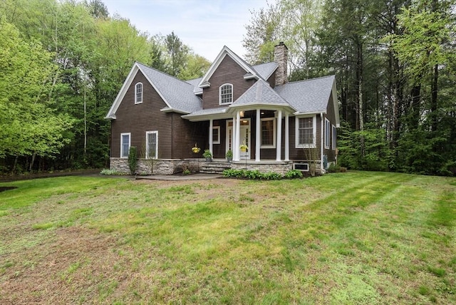 view of front of property with covered porch, a shingled roof, a front lawn, and a chimney