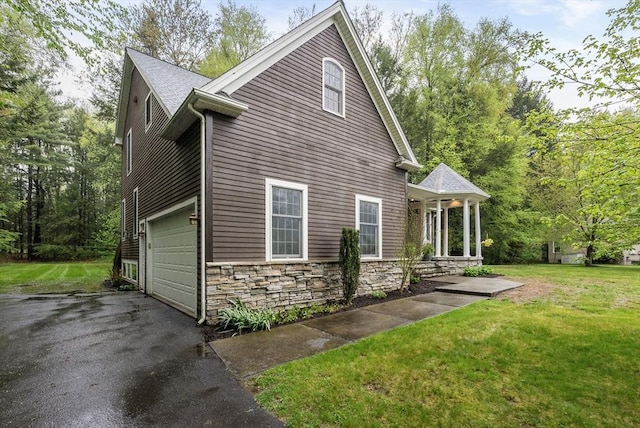 view of side of property with a yard, driveway, a garage, and stone siding