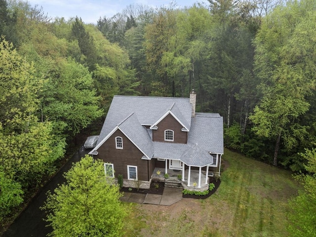 view of front of property featuring a chimney, a front yard, roof with shingles, and a wooded view