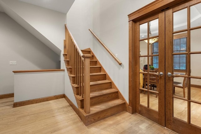 stairs with french doors, wood finished floors, and baseboards