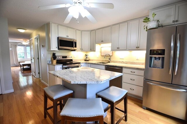 251 Sunderland Rd Unit 251, Worcester, MA 01604 - kitchen featuring stainless steel appliances, a ceiling fan, a kitchen island, light wood finished floors, and light stone countertops