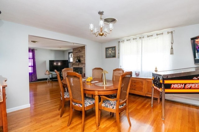 dining room with light wood-style floors, a chandelier, a fireplace, and baseboards