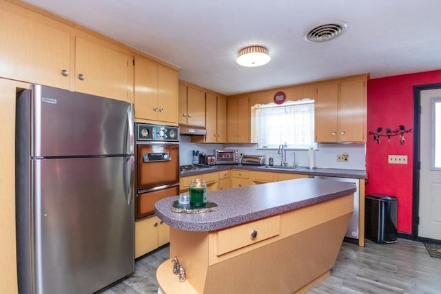 kitchen with stainless steel appliances, a warming drawer, a sink, light wood-style flooring, and dark countertops
