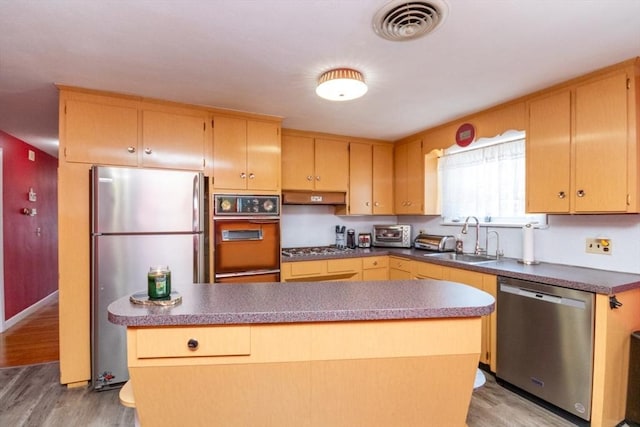 kitchen with stainless steel appliances, a sink, light wood-type flooring, under cabinet range hood, and dark countertops