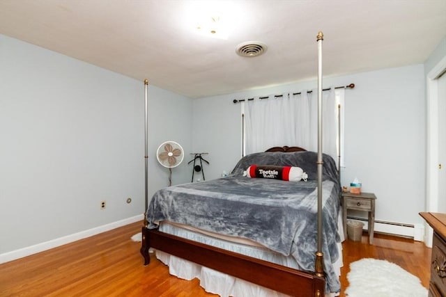bedroom featuring a baseboard heating unit, wood finished floors, and baseboards