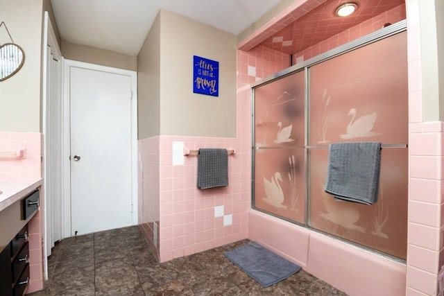 full bath with shower / bath combination with glass door, tile walls, vanity, tile patterned flooring, and wainscoting