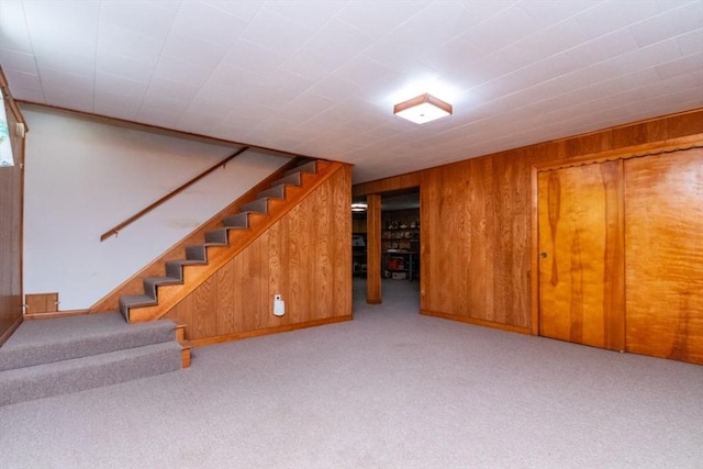 finished basement featuring carpet floors, wood walls, and stairs
