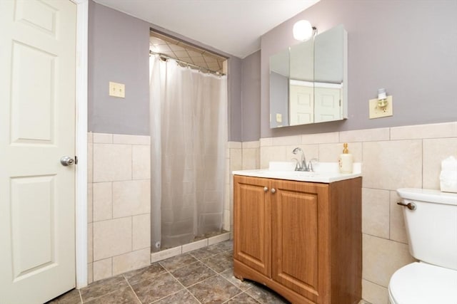 bathroom with tile walls, toilet, tiled shower, vanity, and tile patterned floors