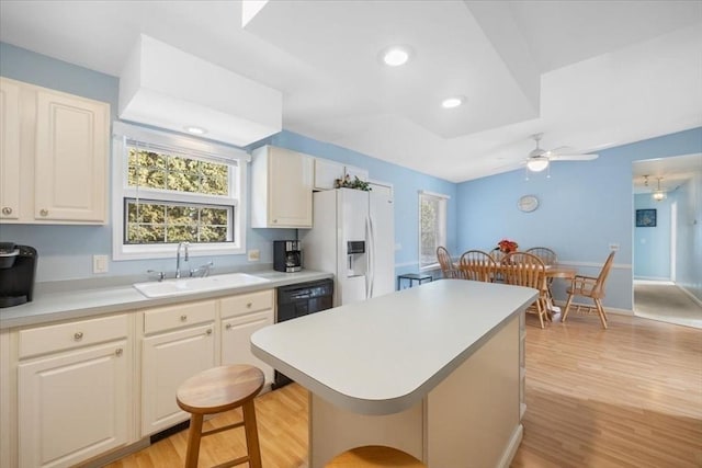 kitchen featuring black dishwasher, sink, a kitchen bar, white refrigerator with ice dispenser, and light wood-type flooring