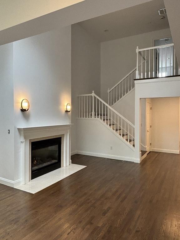unfurnished living room with baseboards, a fireplace with flush hearth, wood finished floors, and stairway