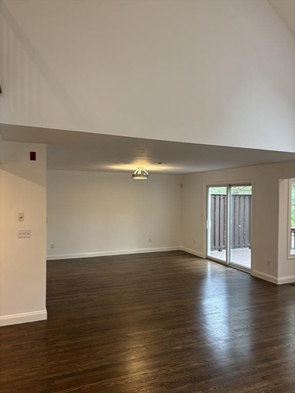 spare room with baseboards, dark wood-style flooring, and lofted ceiling