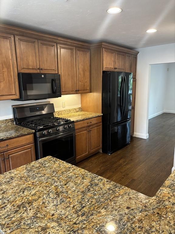 kitchen featuring dark stone counters, brown cabinetry, black appliances, and dark wood-style flooring