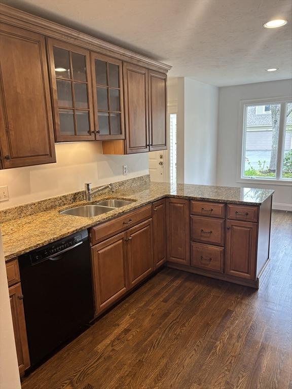 kitchen with dishwasher, a sink, a peninsula, dark wood-style floors, and glass insert cabinets