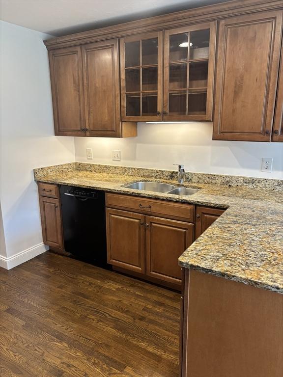 kitchen with black dishwasher, dark wood finished floors, a sink, and light stone counters