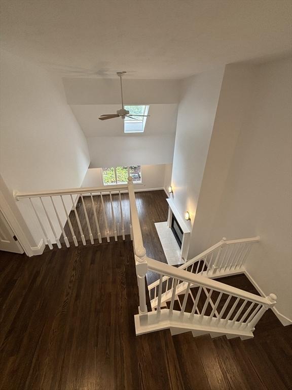 staircase featuring baseboards, a ceiling fan, wood finished floors, and a skylight