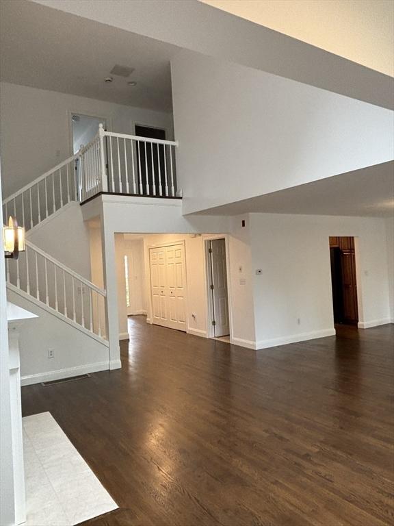 unfurnished living room featuring wood finished floors, baseboards, stairs, and a high ceiling