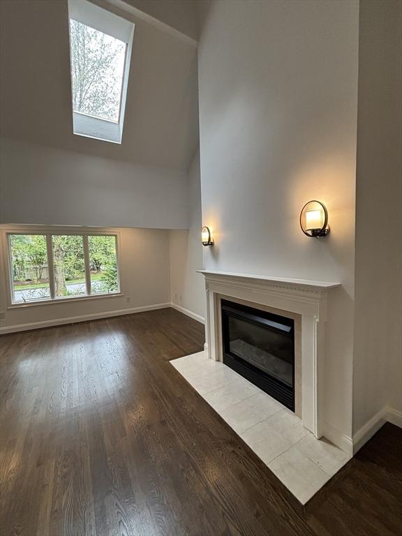 unfurnished living room featuring baseboards, a fireplace, high vaulted ceiling, and wood finished floors