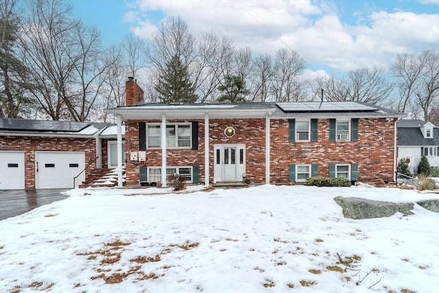 split foyer home with roof mounted solar panels, brick siding, a chimney, and an attached garage