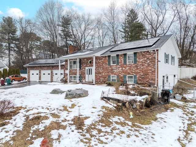 raised ranch with an attached garage, roof mounted solar panels, a chimney, and brick siding