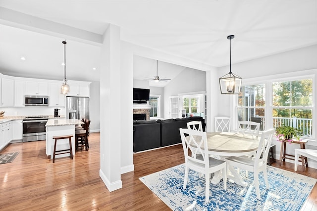 dining room with lofted ceiling with beams, light hardwood / wood-style flooring, and ceiling fan with notable chandelier