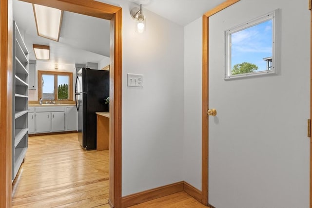 hallway featuring light wood finished floors, baseboards, a healthy amount of sunlight, and a sink