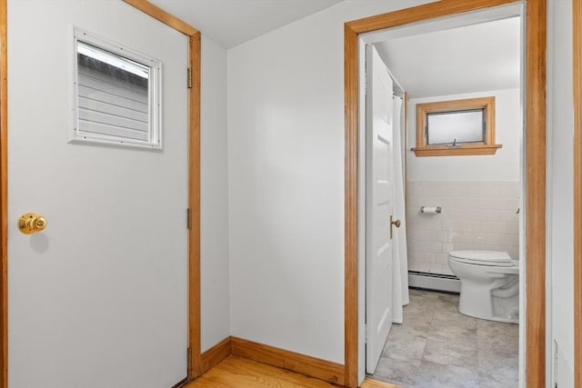 corridor with baseboards, tile walls, and baseboard heating