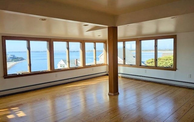 spare room with wood finished floors, a water view, a healthy amount of sunlight, and a baseboard heating unit