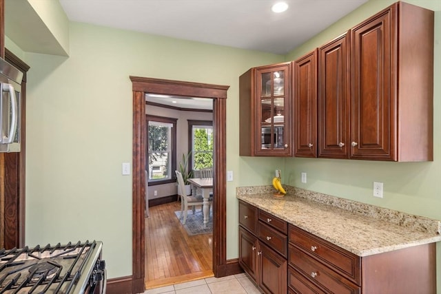 kitchen with light stone countertops, baseboards, glass insert cabinets, range with gas stovetop, and recessed lighting