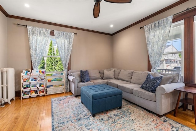 living area with wood-type flooring, ornamental molding, radiator, and a ceiling fan