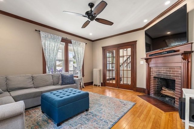 living area with wood-type flooring, ornamental molding, radiator, a brick fireplace, and a ceiling fan