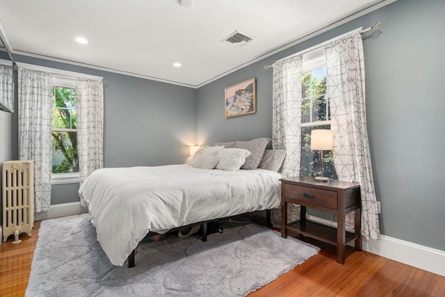 bedroom with visible vents, wood finished floors, baseboards, radiator, and ornamental molding