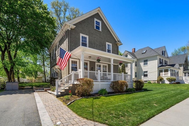 american foursquare style home featuring a porch, driveway, and a front yard